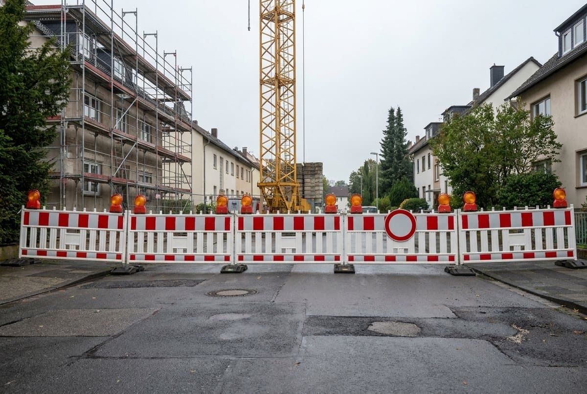 Vollgesperrte Wohnstraße mit Absperrschranken, dahinter ein eingerüstetes Gebäude und der Gittermast eines Baukrans